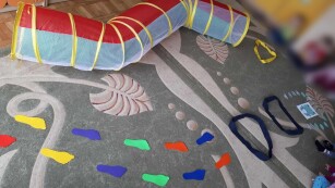 tunel przez który mogą przechodzić dzieci, stopki silikonowe z wypustkami, szarfy rozłożone na dywanie  całość tworzy tor przeszkód dla dzieci.